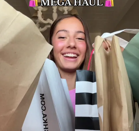 Ragazza sorridente che mostra diverse buste della spesa sotto la scritta «Mega haul»
