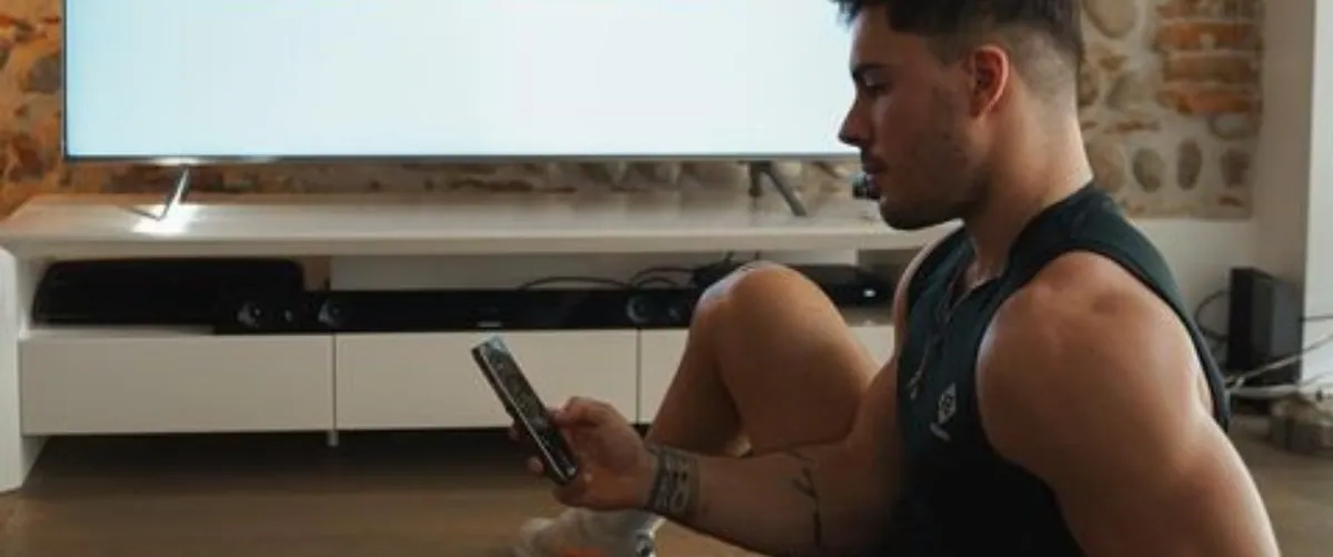 Ragazzo seduto sul pavimento di un soggiorno che guarda lo smartphone davanti a un televisore