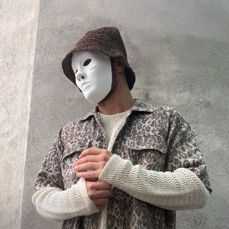 Ragazzo con una maschera bianca, un cappello da pescatore e una camicia leopardata davanti a un muro di cemento