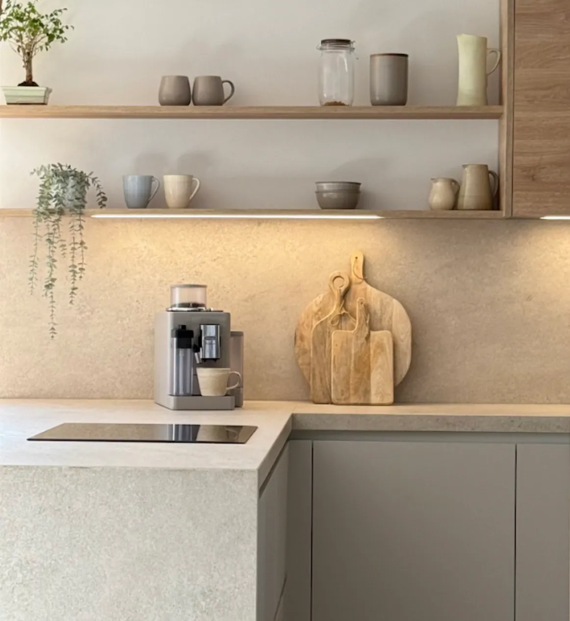 Angolo di una cucina moderna con mensole in legno, tazze in ceramica, una macchina per il caffè e taglieri appoggiati al piano di lavoro