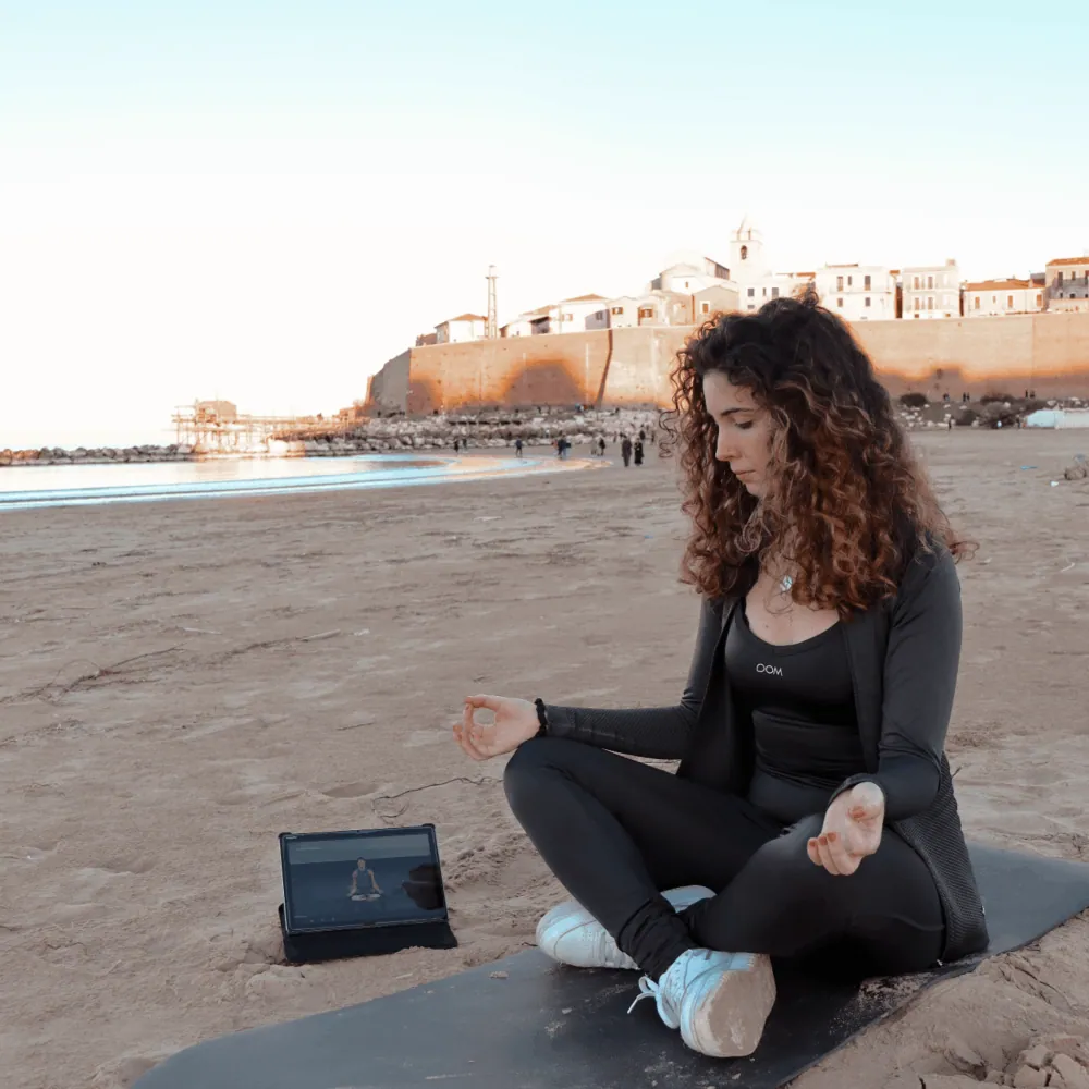 La créatrice Gaia Antenucci médite sur un tapis sur la plage en suivant un cours Virgin Active Revolution sur sa tablette