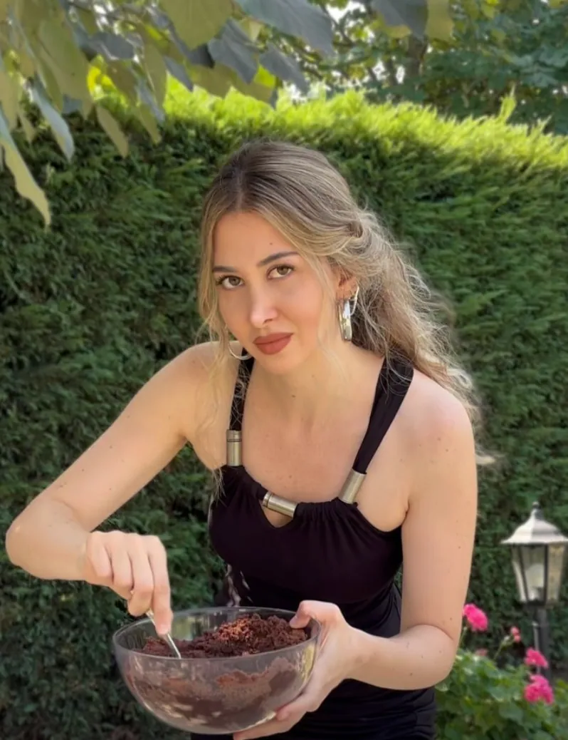 Una creator in giardino mescola un impasto al cacao in una ciotola di vetro guardando in camera
