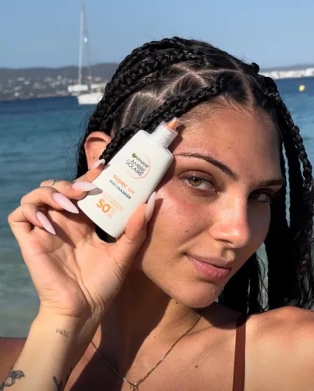 Una creator in spiaggia mostra un flacone di protezione solare Garnier Ambre Solaire SPF 50