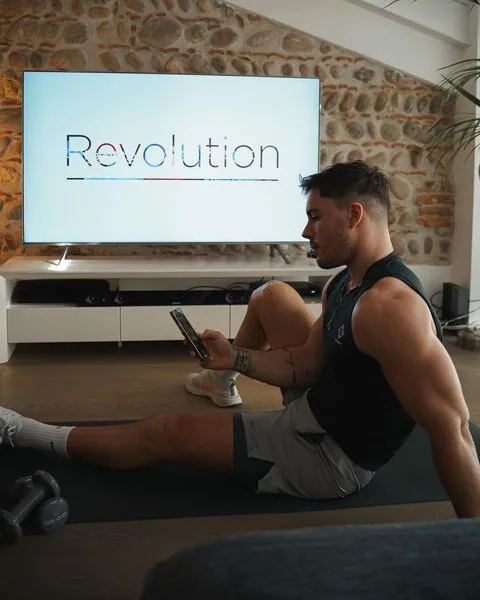 Le créateur Nicholas Cornia assis sur un tapis d’entraînement devant une télévision affichant le logo Revolution de Virgin Active