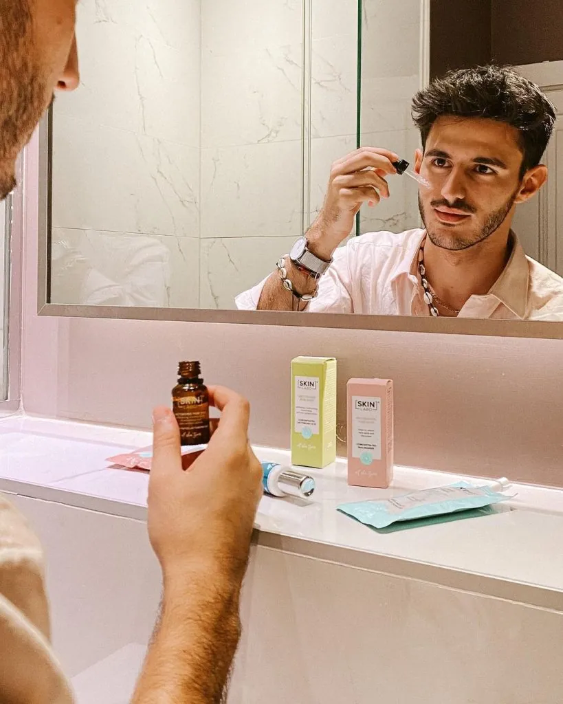Le créateur Alessandro Baffi applique un sérum devant le miroir, avec les produits Skinlabo posés sur le lavabo
