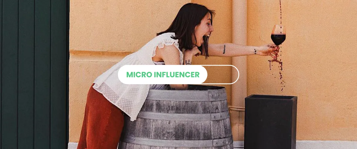 Una micro influencer appoggiata a una botte versa del vino rosso da un calice, con la scritta Micro influencer