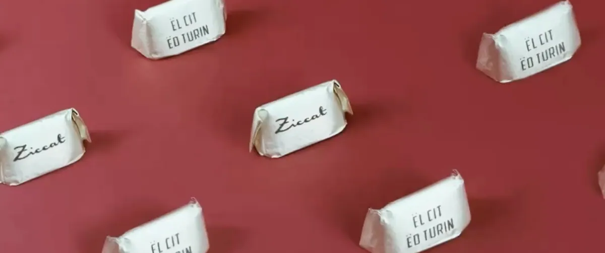 Wrapped sweets printed with Ziccat and «Ël cit ëd Turin» arranged on a red background