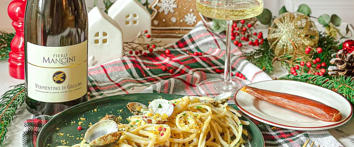 Christmas table with spaghetti and clams, a bottle of Vermentino di Gallura, a glass of white wine and holiday decorations