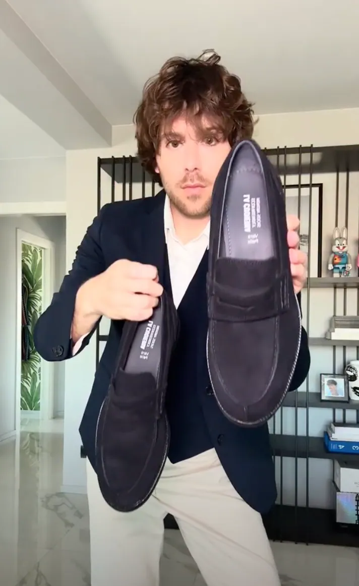 Un créateur présente une paire de mocassins PittaRosso, en les tenant à la main devant l’objectif